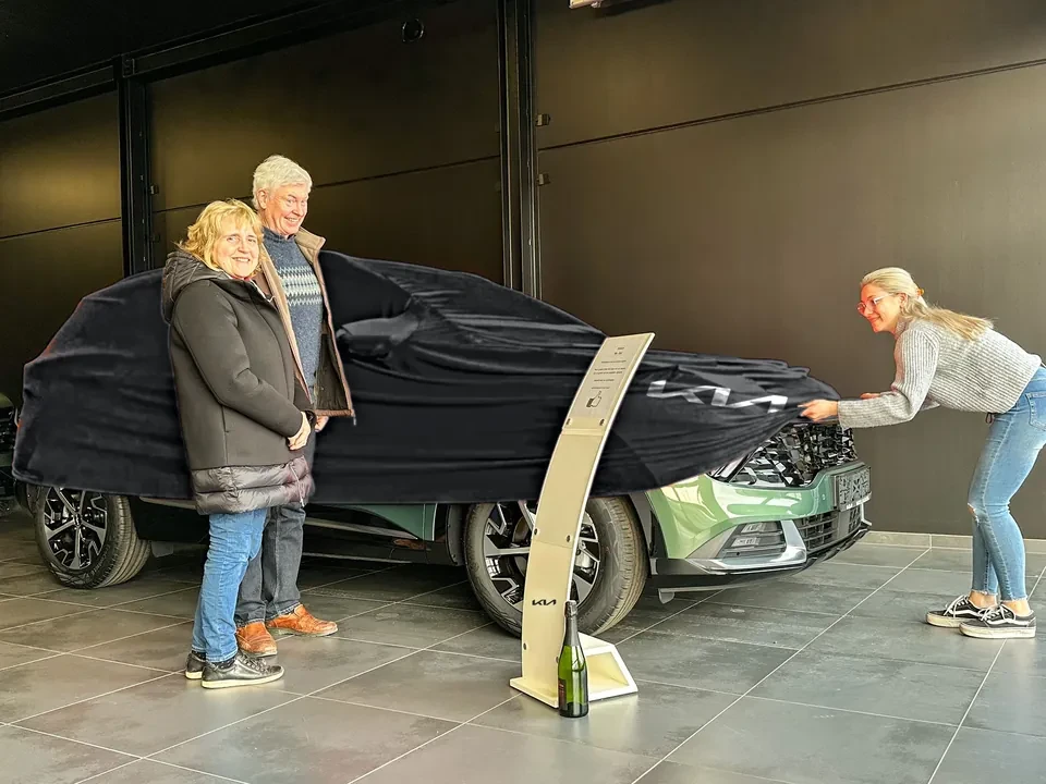 Een klant krijgt haar nieuwe Kia in onze showroom: het zwarte doek met het Kia-logo gaat eraf