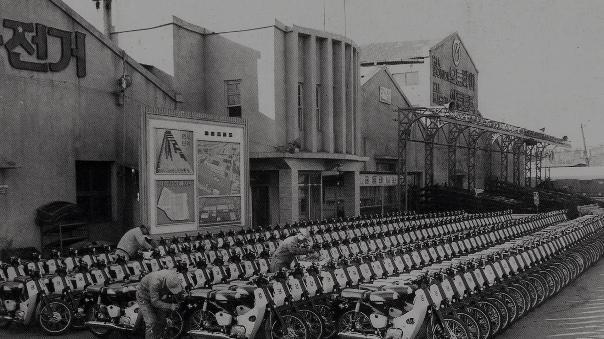 Historische zwart-witfoto van een fabriek van Kia in Korea, met rijen motorfietsen ervoor